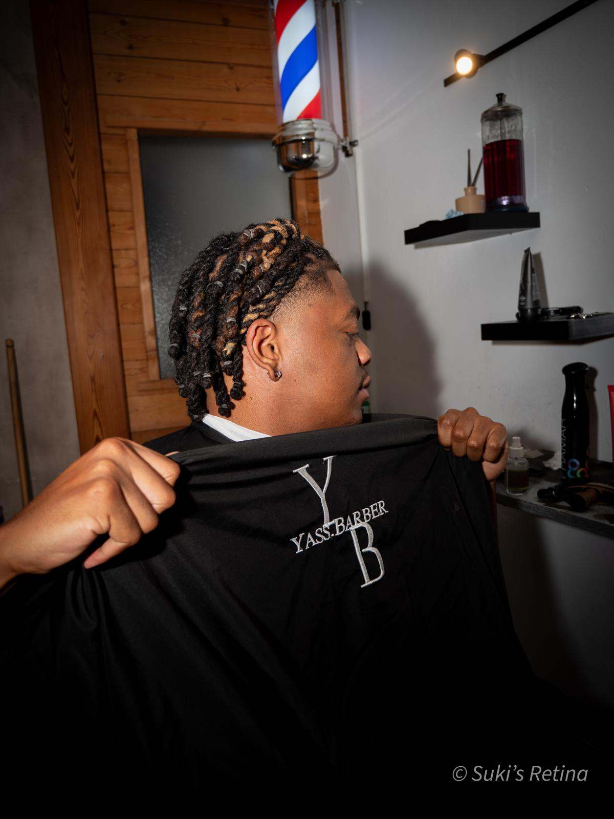 Client dans le barbershop Yass.Barber à Briançon, cape brodée au logo YB